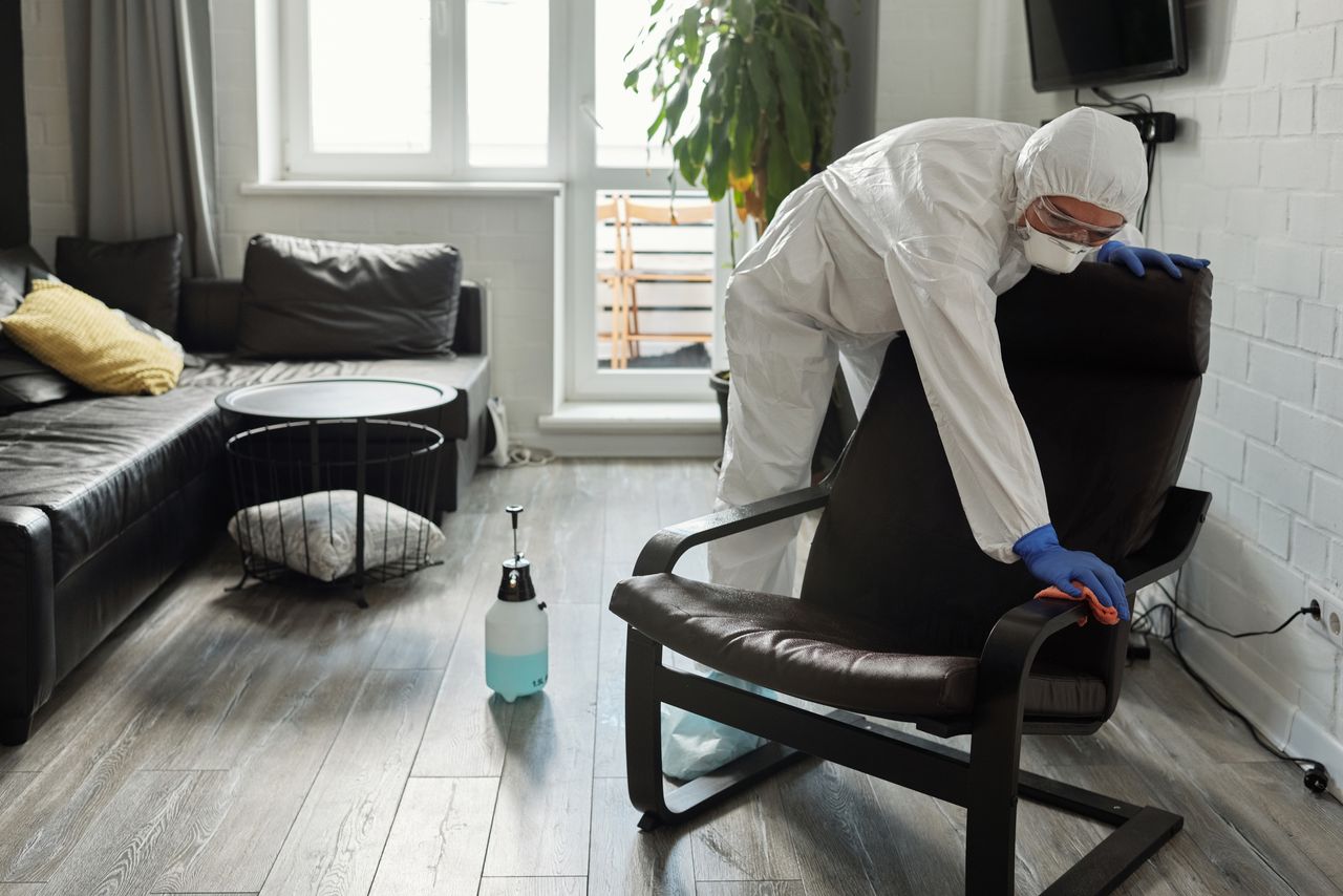 services-02 A person in PPE cleaning a modern living room, emphasizing safety and hygiene.