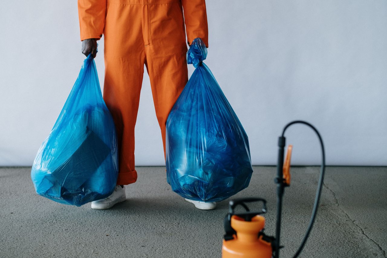 services-01 Sanitation worker in orange overalls holding blue trash bags indoors for waste management.